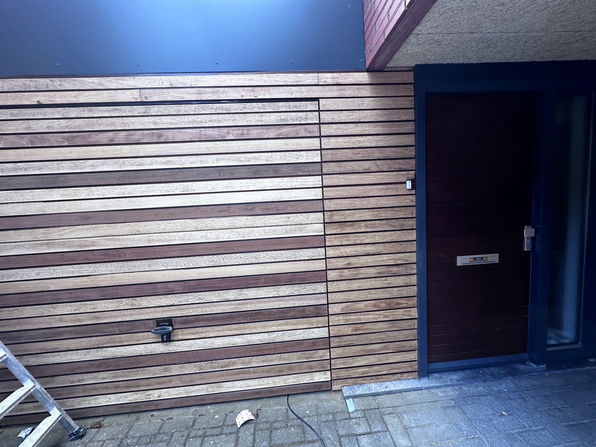 Afgewerkte houten gevelbekleding naast een donker gebeitste voordeur