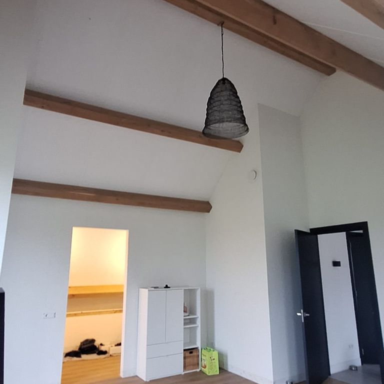 Een afgewerkte kamer met witte wanden onder zichtbare eiken balken