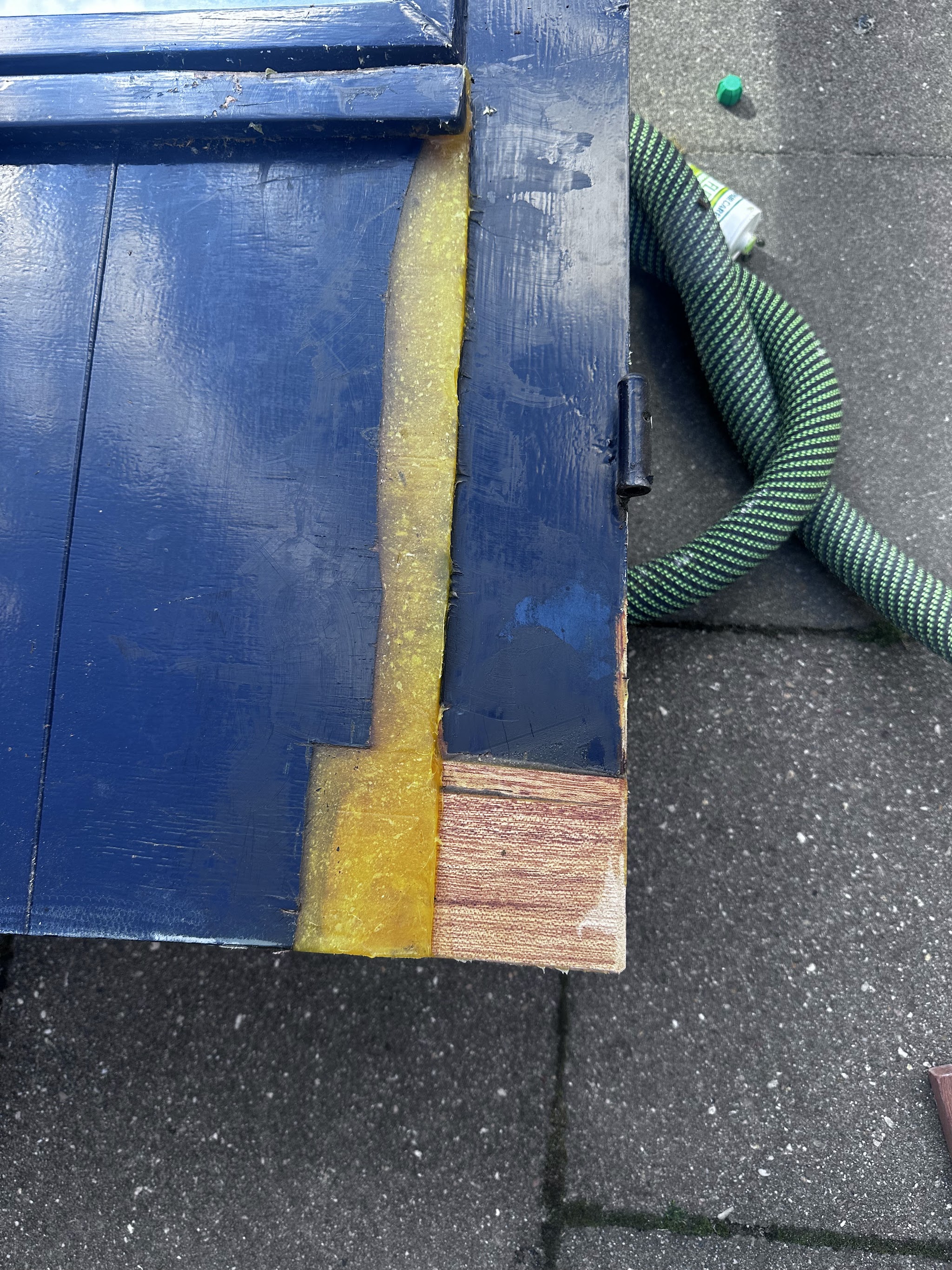 Een weggerotte hoek van een blauwe deur waarin een nieuw stuk hout is ingezet